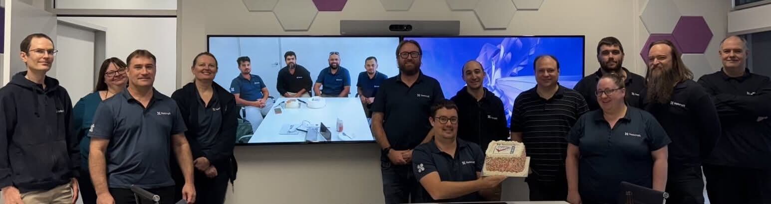 Netcraft's Adelaide team celebrating the ISO 9001 certification
with a cake, joined by remote colleagues on the boardroom screen